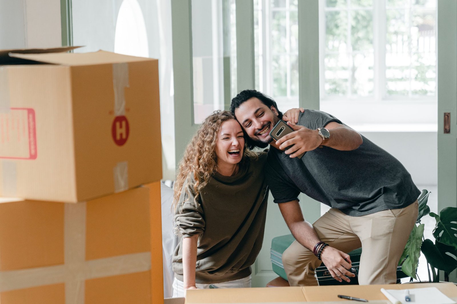 Pareja joven feliz haciéndose una foto entre cajas de mudanza en su primera vivienda